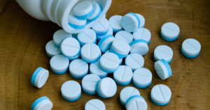 Blue and white round tablets spilling from a white bottle onto a wooden surface.