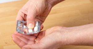 Close-up of hands holding a blister pack of white pills on a wooden surface