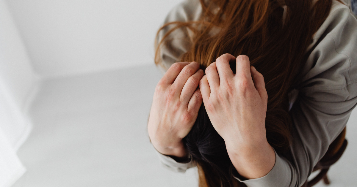 Person with long red hair holding their head with both hands, suggesting stress or frustration outside light room.