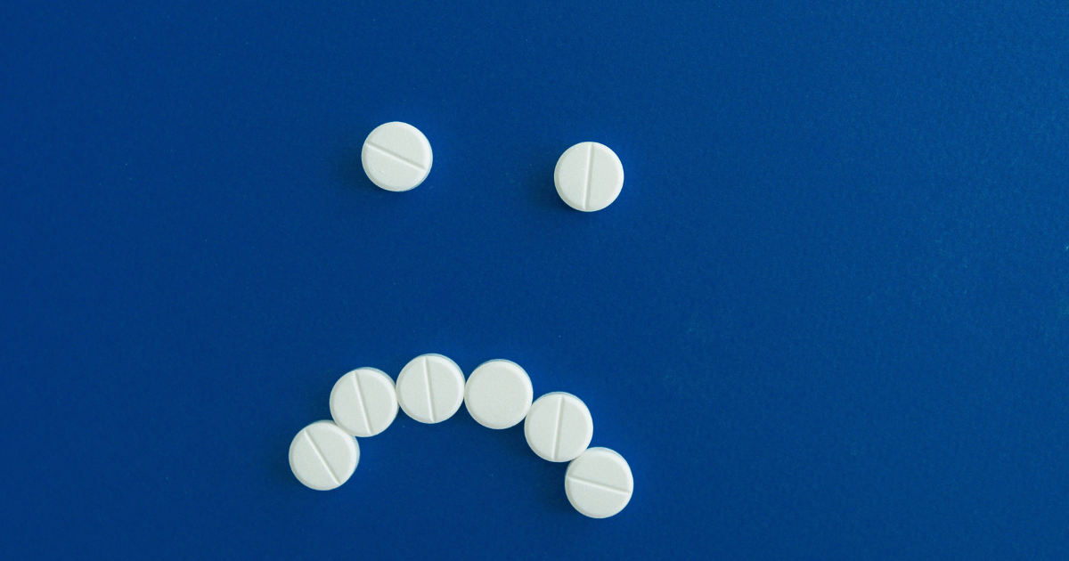 Two white round pills placed as eyes above a curved row of pills forming a smile on a blue background.