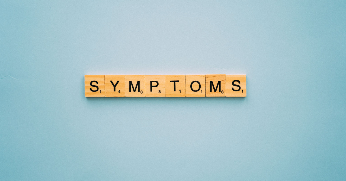 Wooden letter tiles spell the word 'SYMPTOMS' on a light blue background.